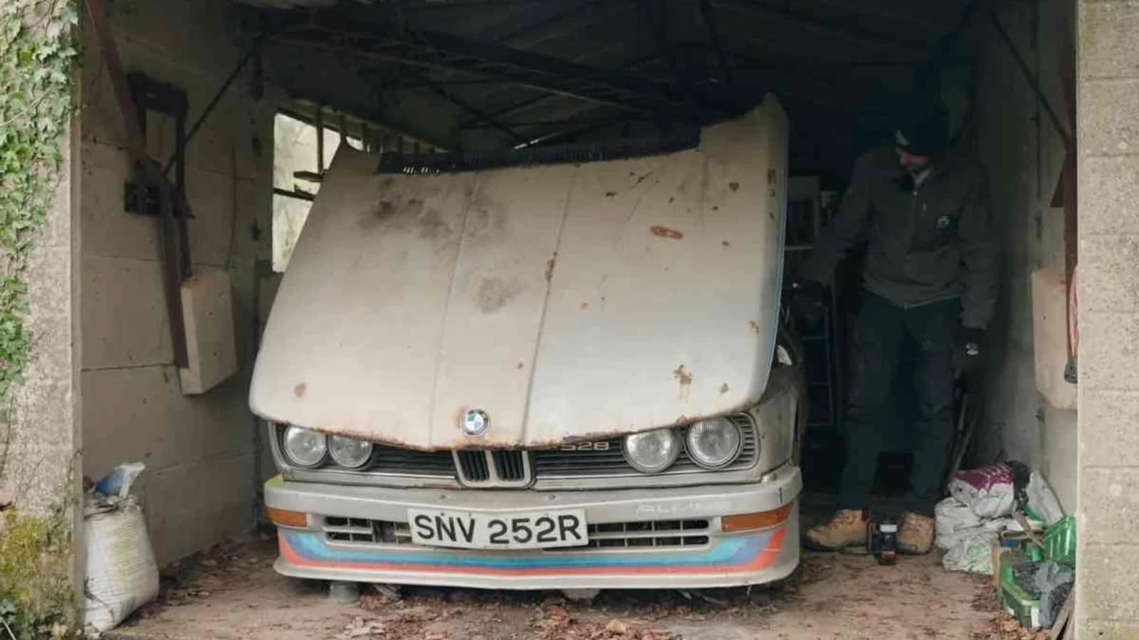 Automobile classica bianca parcheggiata in un vecchio garage tra muri e oggetti d'epoca.