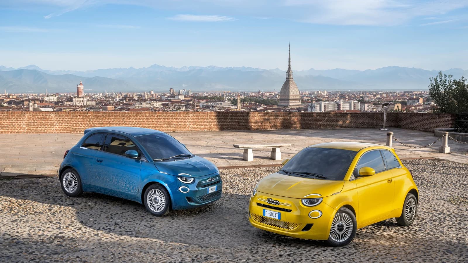 Fiat 500 ibride azzurra e gialla parcheggiate in una piazza cittadina.