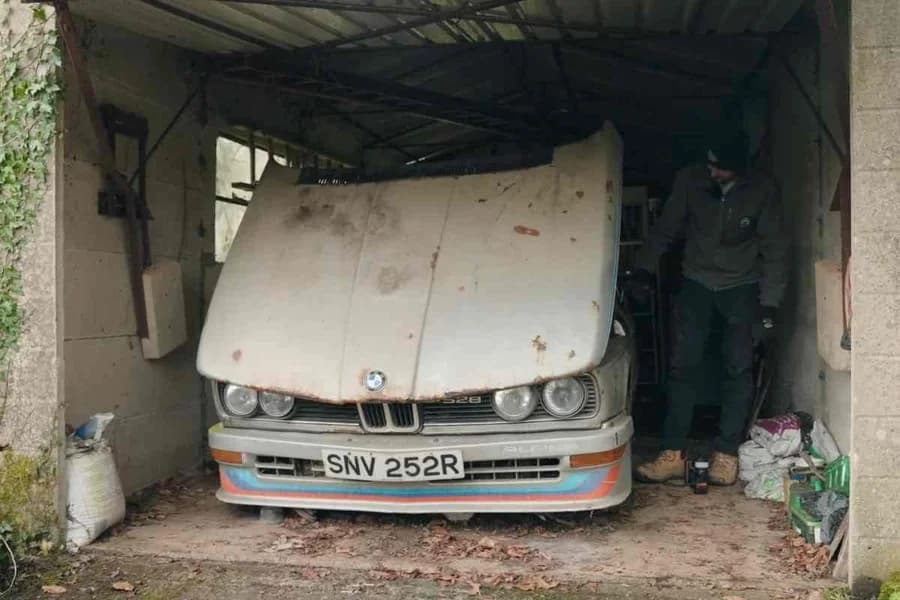 Automobile classica bianca parcheggiata in un vecchio garage tra muri e oggetti d'epoca.